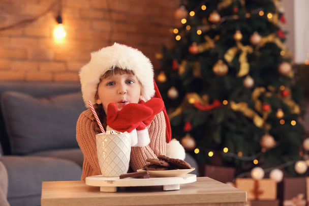 Roztomilá holčička v Santa čepice s horkou čokoládou a cookies doma na Štědrý den - Fotografie, Obrázek