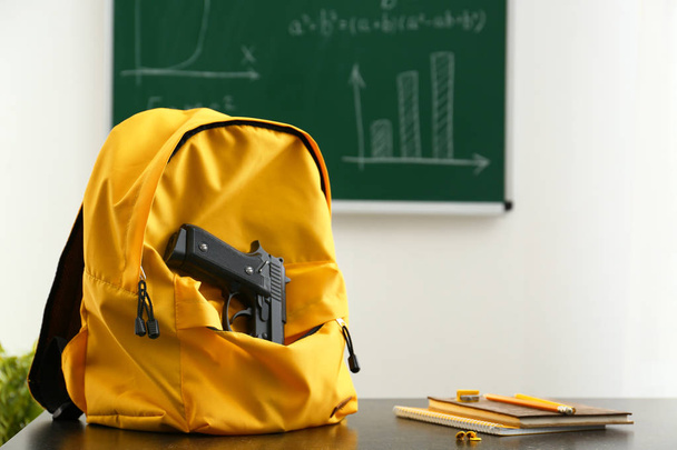 Backpack with pistol on table in classroom. No guns in school - Φωτογραφία, εικόνα