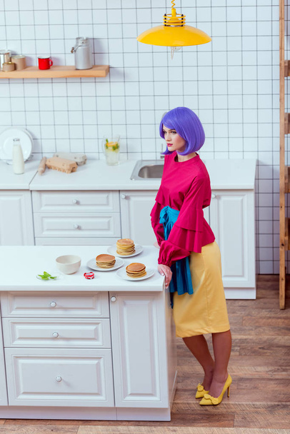 housewife with purple hair and colorful clothes posing near kitchen counter with pancakes - Φωτογραφία, εικόνα