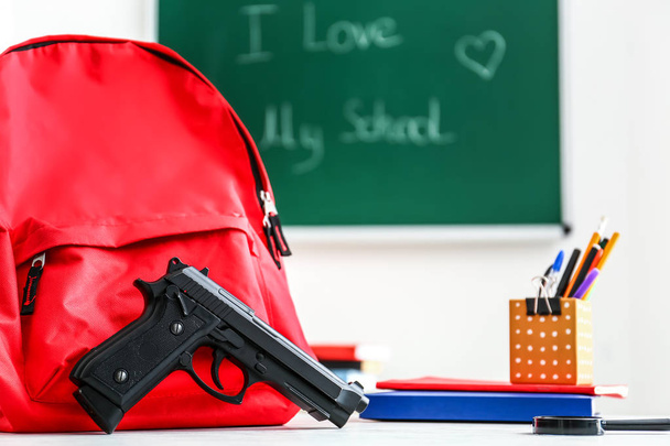 Backpack, pistol and stationery on table in classroom. No guns in school - Foto, Imagem