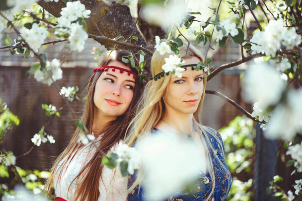 Portrait of young beautiful women smiling in the flowered garden in the spring time. Almond flowers are blooming. The girl is dressed stylishly, jewelry on her head. - image - Фото, изображение