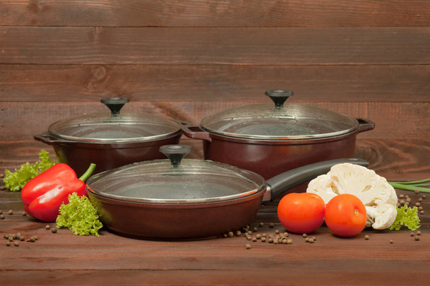 Aluminum non-stick cookware with vegetables on wooden background - Photo, Image