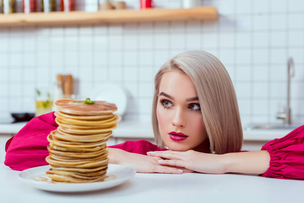 beautiful girl looking at plate of delicious pancakes in kitchen - Foto, imagen