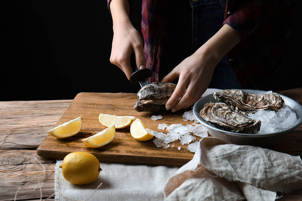 Woman opening raw oyster with knife at table - Foto, imagen