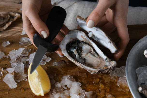Woman opening raw oyster with knife at table, closeup - Photo, Image