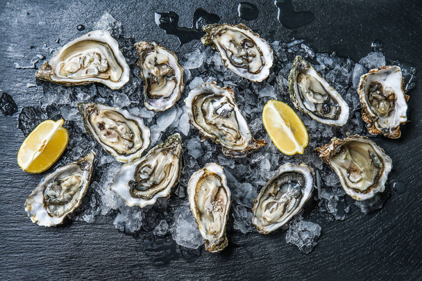 Tasty raw oysters with ice and lemon on dark background - Foto, Imagem