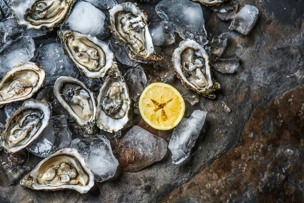 Leckere rohe Austern mit Eis und Zitrone auf dunklem Hintergrund - Foto, Bild