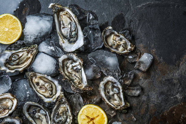 Lekkere rauwe oesters met ijs en citroen op donkere achtergrond - Foto, afbeelding