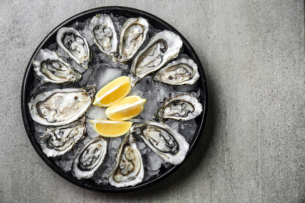 Plateau avec huîtres froides savoureuses et citron sur table grise
 - Photo, image