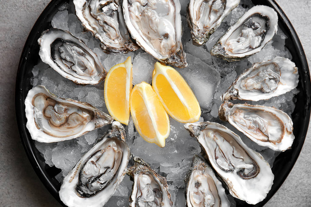 Tray with tasty cold oysters and lemon on grey table - Photo, Image