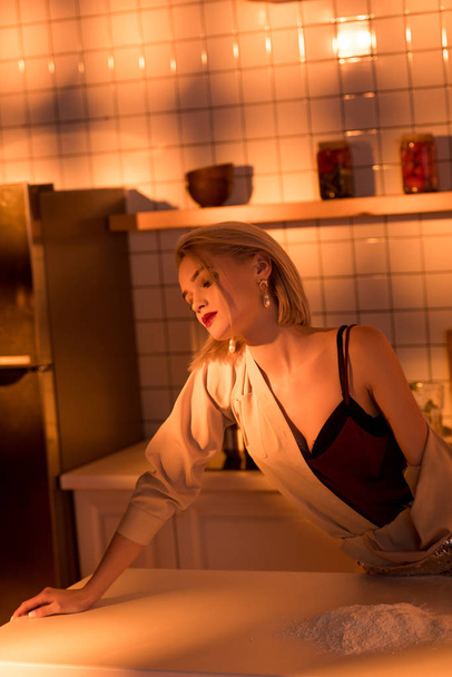 messa a fuoco selettiva di elegante casalinga appoggiata al bancone mentre cucina in cucina con luce arancione
 - Foto, immagini