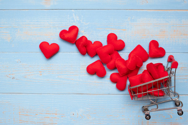Top view red heart shape decoration with mini shopping cart on blue wooden table background. love romantic shopping and Valentine Day holiday Concept - Фото, изображение