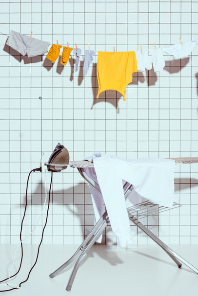  hanging clothes and ironing board with white tile on background in bathroom - Foto, imagen