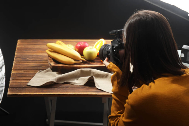 Young woman taking picture of tasty fruits in professional photo studio - Fotó, kép