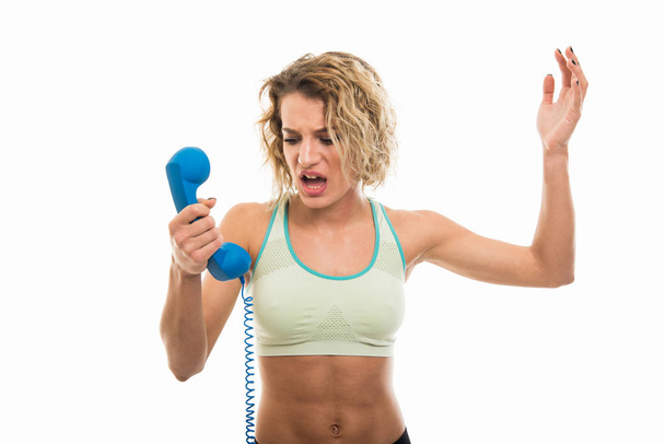 Portrait of beautiful young fit girl screaming at telephone receiver isolated on white background with copy space advertising area - Photo, image