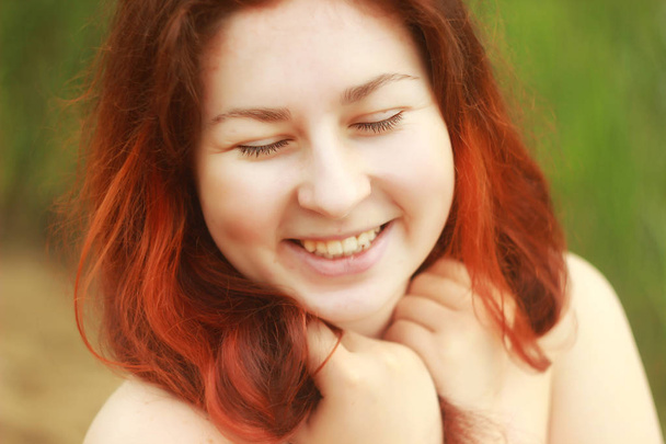 Μια νεαρή γυναίκα Καυκάσιος λευκό χαρωπά χαμόγελα και γέλια με χαριτωμένα λακκάκια στα μάγουλα της. Έχει τα μακριά κόκκινα μαλλιά και κλειστά τα μάτια. - Φωτογραφία, εικόνα