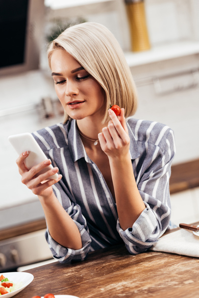 selective focus of attractive woman holding tomato and smartphone - Foto, immagini
