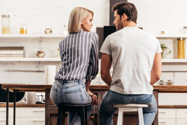 rear view of boyfriend and attractive girlfriend sitting on chairs in kitchen - Foto, afbeelding