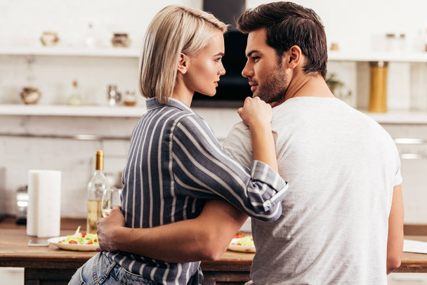 beautiful young couple looking at each other and hugging in kitchen - Фото, зображення