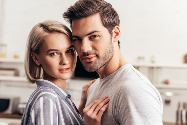 selective focus of handsome boyfriend and attractive girlfriend hugging and looking at camera - Fotografie, Obrázek