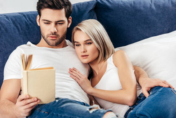 selective focus of attractive girlfriend and handsome boyfriend laying and reading book - Foto, Bild