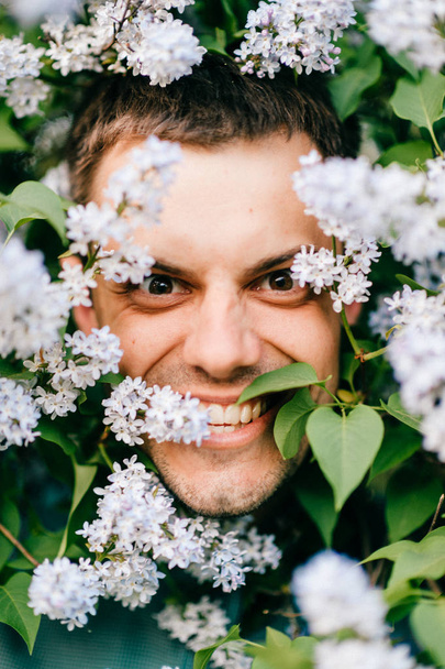 Closeup portrait of young man in beautiful lilac bushes - 写真・画像