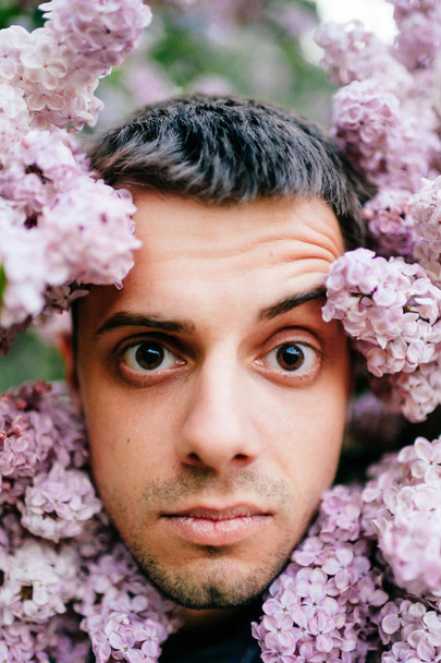 Closeup portrait of young man in beautiful lilac bushes - Фото, изображение