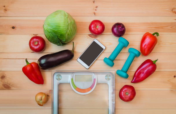Verse groenten, groene halters, smarthone en gewicht schaal. Gezonde voeding-concept. Bovenaanzicht, kopie ruimte. - Foto, afbeelding