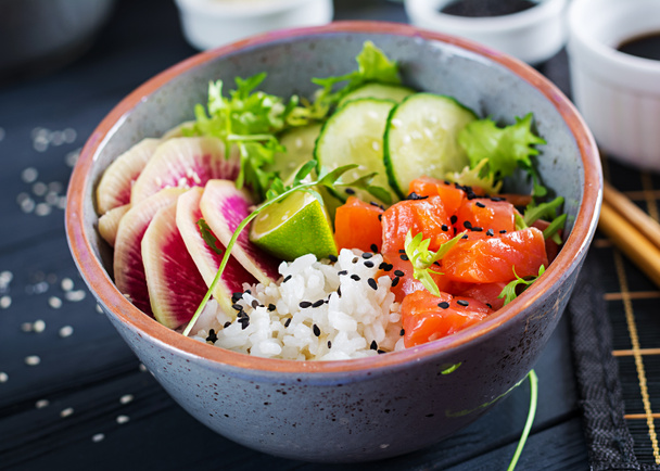 Hawaiian zalm vissen poke kom met rijst, komkommer, radijs, sesamzaadjes en kalk. Buddha bowl. Dieet voeding. - Foto, afbeelding