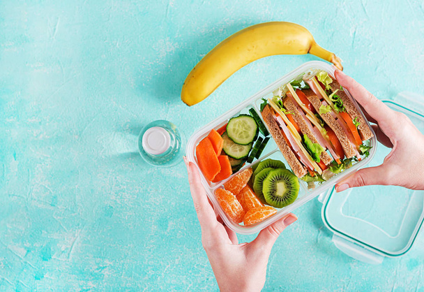 Lunchbox in handen. School de doos van de lunch met sandwiches, fruit, water en fruit op tafel. Gezond eten gewoonten concept. Flat lag. Bovenaanzicht - Foto, afbeelding