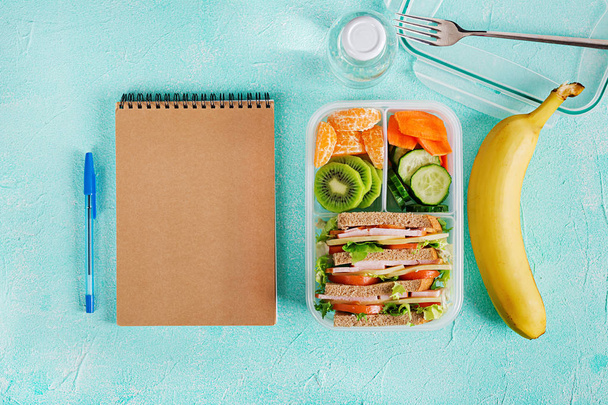 School lunch box with sandwiches, vegetables, water and fruits on table. Healthy eating habits concept. Flat lay. Top view - Photo, Image