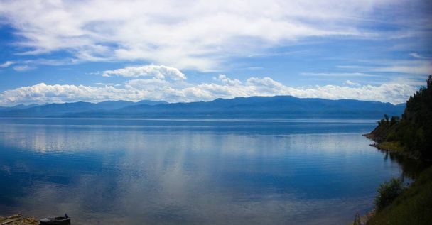 Summer landscape with boat on lake Baikal. Awe view on mountain range, sky and forest. Coastline of most deep clear lake in world. Background for wild travel and adventure trip - Photo, Image