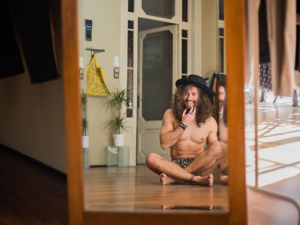 Smiling naked man in hat sitting in front of mirror  - Valokuva, kuva
