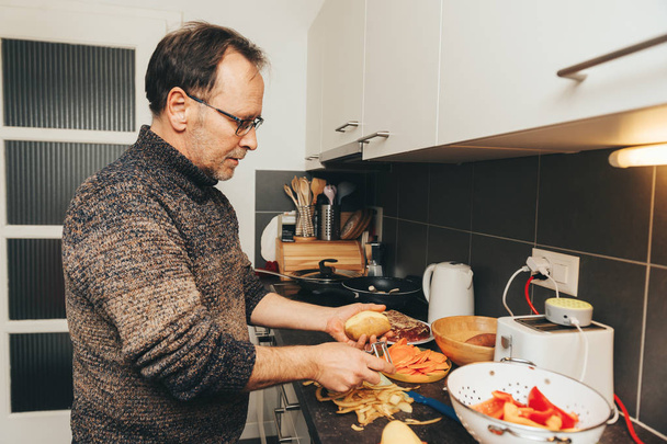 Középkorú férfi főzés vacsora a konyhában, leválik a burgonya hámozó - Fotó, kép