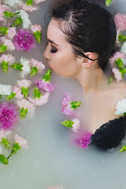 mooie sexy triest jonge slanke brunette vrouw in spa - badkamer met water en bloemen - Foto, afbeelding