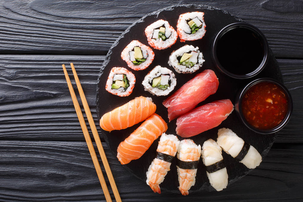 Comida japonesa de sushi. Maki ands rola com atum, salmão, camarão, caranguejo e abacate com dois molhos close-up em um prato de ardósia. vista superior horizontal a partir de abov
 - Foto, Imagem