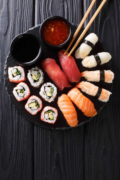 Japanese sushi food. Maki ands rolls with tuna, salmon, shrimp, crab and avocado with two sauces close-up on a slate plate. Vertical top view from abov - Фото, изображение