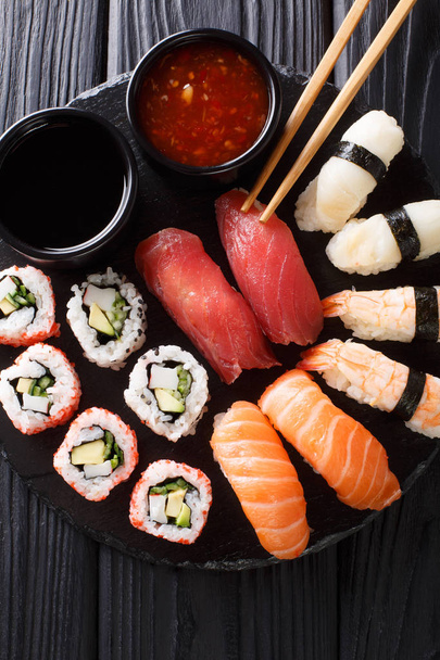 Joukko tuoretta maki, uramaki ja nigiri sushia, tarjoillaan mustalla lautasella lähikuva. Pystysuora ylhäältä katsottuna abov
 - Valokuva, kuva