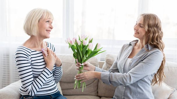 Daughter presenting bouquet of tulips to senior mother - Foto, imagen