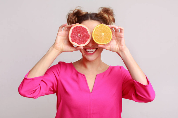 Woman covering eyes with citrus fruits, grey background - Foto, Bild