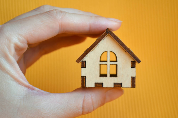 Дерев'яна модель іграшкового будинку в руці жінки на жовтому тлі, вид спереду
 - Фото, зображення
