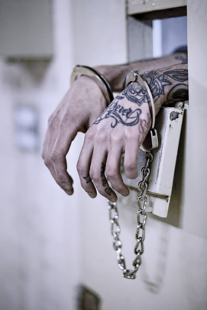 τα χέρια του φυλακισμένου tattoed κλειδωμένα με handcuff στο παρασκήνιο φυλακή - Φωτογραφία, εικόνα