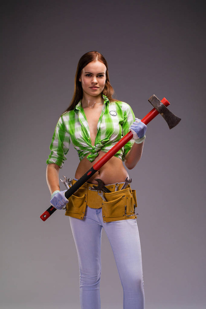 Satisfaction project. Sexy beautiful brunette girl holding an ax, isolated over gray background - Foto, Imagen