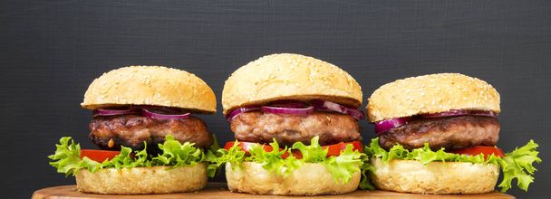 Burgers with beef cutlets on wooden board over black background, side view. Close-up. - Photo, Image