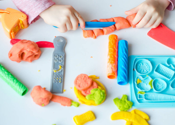 Child's hands with colorful clay. Child playing and creating vagetables from play dough. Girl molding modeling clay. Homemade clay - Photo, Image