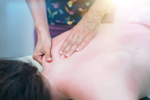 Fisioterapeuta masajeando espalda y hombro de mujer contra bengalas de lentes
  - Foto, Imagen