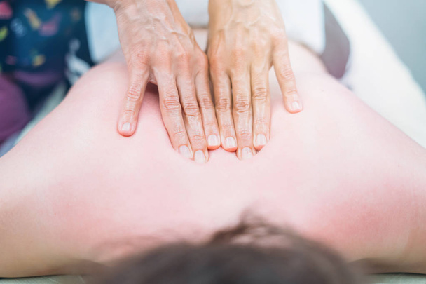 Fysiotherapeut masseren van rug en schouders van de vrouw tegen de lens flare  - Foto, afbeelding