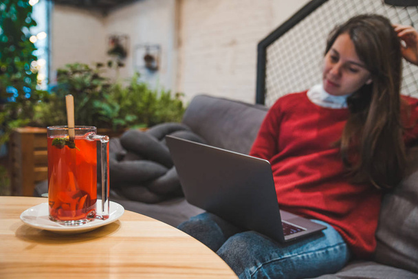 fiatal felnőtt nő dolgozik a laptop a kávézóban csésze gyümölcs tea ivás közben. modern életmód - Fotó, kép