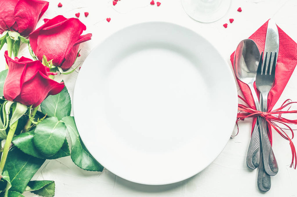 Valentine's Day décor de table romantique avec des roses rouges, assiettes, couverts sur fond blanc. Assiette vide. Mise en page de conception de maquettes pour votre texte. Concept de Valentines d'amour. Espace de copie. Vue de dessus. Pose plate
. - Photo, image