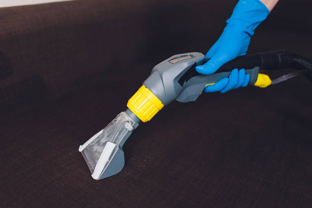Sofa chemical cleaning with professionally extraction method. Upholstered furniture. Early spring cleaning or regular clean up. Dry cleaners in blue protective glove employee removing dirt from - Foto, Bild